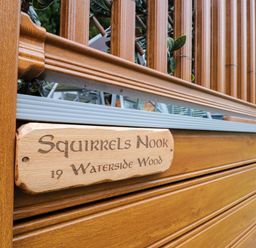 A wooden fence with a carved wooden sign that reads Squirrels Nook 19 Waterside Wood