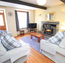 A living room with two sofas a wooden coffee table a rug a television a fireplace and wooden flooring at Hafan Cottage in Beddgelert