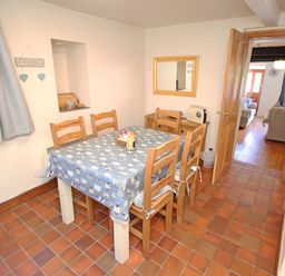 A dining room with a table covered by a blue tablecloth and six wooden chairs at Hafan Cottage in Beddgelert