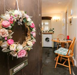 A floral wreath on a door with a small dining table and chairs in a kitchen at Gardeners Cottage in Millom Cumbria