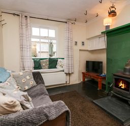 A living room with a wood burning stove sofa cushions window seat and television at Gardeners Cottage in Millom Cumbria
