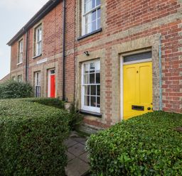 A row of brick cottages with a yellow door and a red door and trimmed hedges outside 3 Albion Cottages Walberswick