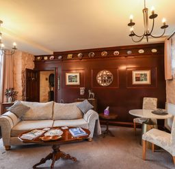 A sitting room with a sofa, two side tables, a coffee table, two chairs at a round table, and a dark wood paneled wall at The Barn in Middleton near Ponteland