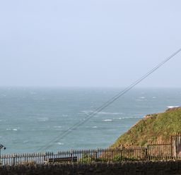 A view of the ocean with a metal fence and a viewing telescope on a stone wall by a grassy hillside at 31 Cliff Edge in Newquay