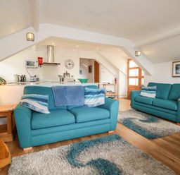 A living room with two teal sofas and patterned rugs at Harbour Light in Boscastle