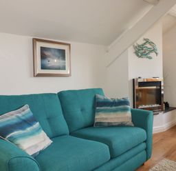 A turquoise sofa with striped cushions a wall-mounted fish decoration and a fireplace in a living room at Harbour Light in Boscastle