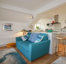 A living room with a blue sofa and pillows next to a kitchen with a stool at Harbour Light in Boscastle