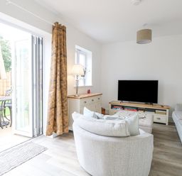 A living room with gray sofas a television on a stand and glass doors leading to a garden at The Hollies in Norwich