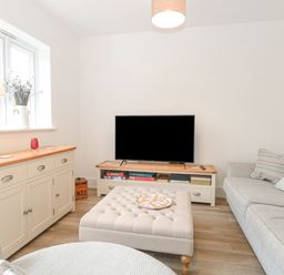 A living room with a large television on a wooden stand a beige ottoman in front of a sofa and a sideboard with a lamp and vase by a window at The Hollies in Norwich