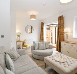 A living room with a gray sofa a round chair an ottoman and a sideboard with lamps and curtains at The Hollies in Norwich