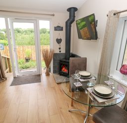 A dining area with a round glass table set for two next to a wood burning stove and double glass doors in Garden View Pembroke