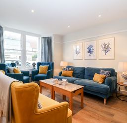 A living room with blue and yellow chairs a wooden coffee table and framed artwork on the wall at Fawcett Cottage in Aldeburgh