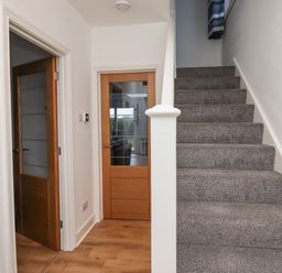 A hallway with wooden doors and a carpeted staircase at Maywood in Seahouses