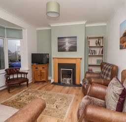 A living room with leather chairs a wooden cabinet a fireplace and a bookshelf at Maywood in Seahouses
