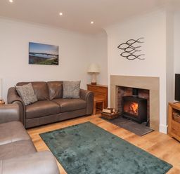 A living room with two leather sofas a fireplace with fire a wooden TV stand and a blue rug at Maywood in Seahouses