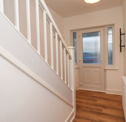 A hallway with a white staircase and a door with frosted glass at Maywood in Seahouses