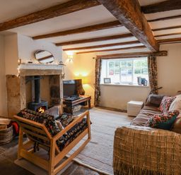 A living room with exposed wooden beams a fireplace a sofa and a wooden armchair at Lythe Cottage in Lythe