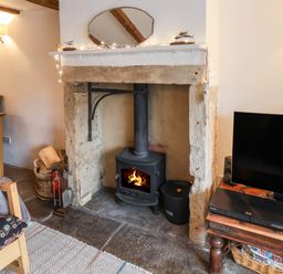 A fireplace with a wood-burning stove and fire in a living room at Lythe Cottage in Lythe