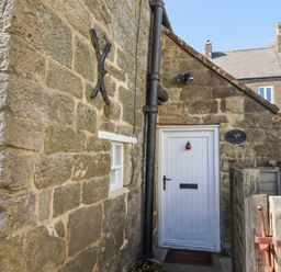 The stone exterior of a cottage with a white wooden door and small window at Lythe Cottage in Lythe