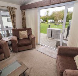 A living room with brown armchairs and a coffee table looking out to a garden through sliding glass doors at Lakeside Haven in Carnforth