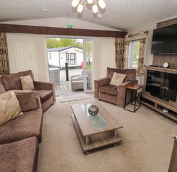 A living room with brown sofas glass coffee table wall mounted tv and sliding glass doors at Lakeside Haven in Carnforth
