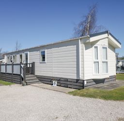 A white mobile home with a deck and steps in a park setting at Lakeside Haven in Carnforth