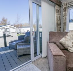 A sofa with a patterned cushion next to sliding glass doors leading to a patio with two wicker chairs at Lakeside Haven in Carnforth