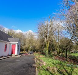 A white house with red windows and door next to a driveway and trees at Kyleatunna Cottage in Ennis County Clare