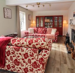 A living room with two patterned sofas a wooden bookshelf and a fireplace at Kyleatunna Cottage in Ennis County Clare