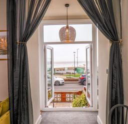 A room with black curtains framing an open window showing a view of parked cars and the beach at Apt 3 @ Hunter's Quay in Bridlington