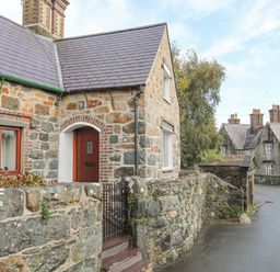 A stone house with a wooden door and fenced garden next to a stone wall along a street at 5 The Crescent in Caernarfon