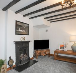 A living room with a fireplace television on a wooden stand table with a lamp and artwork at 5 The Crescent in Caernarfon