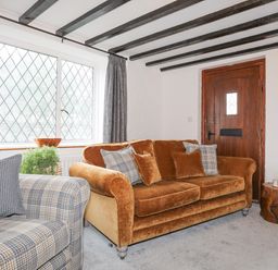 A living room with a brown sofa and a plaid armchair near a wooden door and window at 5 The Crescent in Caernarfon