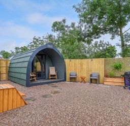A small pod cabin with a wooden hot tub and outdoor seating area with grill in a fenced garden at Heron Pod in Nantmawr near Trefonen