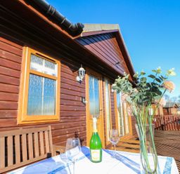 A wooden deck with a table set with a bottle and glasses outside a cabin at The Fairhaven in Tunstall near Catterick North Yorkshire