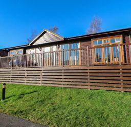 A wooden cabin with a fenced porch and green lawn at The Fairhaven in Tunstall near Catterick North Yorkshire