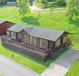 An aerial view of a wooden lodge with a fenced deck and a gravel driveway surrounded by grass at The Fairhaven in Tunstall near Catterick North Yorkshire