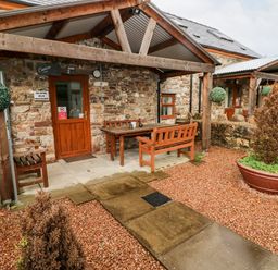 An outdoor seating area with wooden benches and a table under a wooden roof at Barn 2 in Ystradgynlais