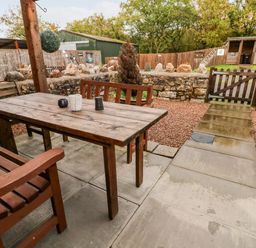 An outdoor patio area with a wooden table and benches surrounded by stone walls and a wooden gate at Barn 2 in Ystradgynlais