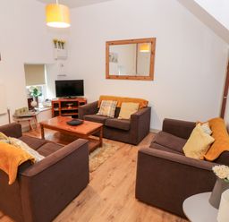 A living room with three brown sofas cushions a wooden coffee table a TV on a stand and a wall mirror at Barn 2 in Ystradgynlais