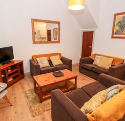 A living room with brown sofas, a wooden coffee table, a television on a wooden stand, and wall art at Barn 2 in Ystradgynlais