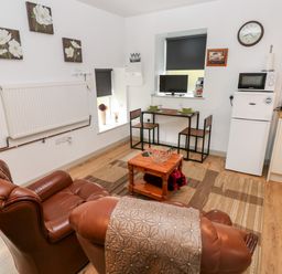 A living area with two leather chairs a wooden table with two chairs a small fridge and microwave at Barn 3 Cwm-twrch Isaf near Ystradgynlais