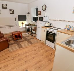 A kitchen and living area with leather armchairs a dining table small refrigerator and stove at Barn 3 Cwm-twrch Isaf near Ystradgynlais