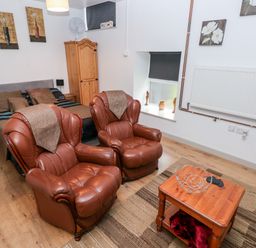 A bedroom with two brown leather armchairs next to a wooden coffee table and a double bed at Barn 3 in Cwm-twrch Isaf near Ystradgynlais