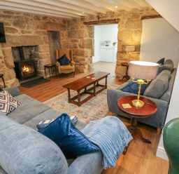 A living room with stone walls a wood burning stove sofas a wooden coffee table and table lamps at The Old Post Office in Praze-An-Beeble