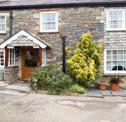 Stone cottage exterior with wooden door bushes and potted plants at Mill Cottage in St Neot