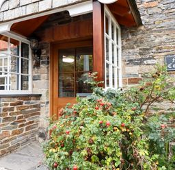 An entrance door with windows on both sides and a bush with red berries outside at Mill Cottage in St Neot