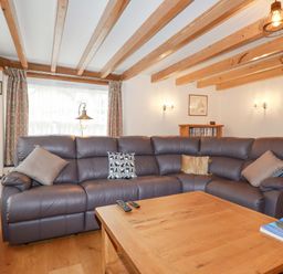 A living room with a large leather sectional sofa and wooden coffee table at Mill Cottage in St Neot
