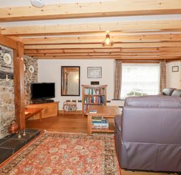 A living room with exposed wooden beams stone fireplace and leather sofa at Mill Cottage in St Neot