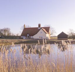A house with a tiled roof and chimney near a pond with reeds at West House Farm in Leiston